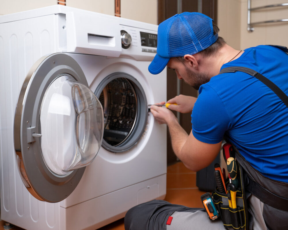 Working man plumber repairs a washing machine in home. Washing machine installation or repair. plumber connecting appliance.