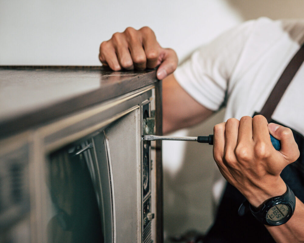 The mechanic uses a screwdriver to tighten the screws on the TV. Selective focus.