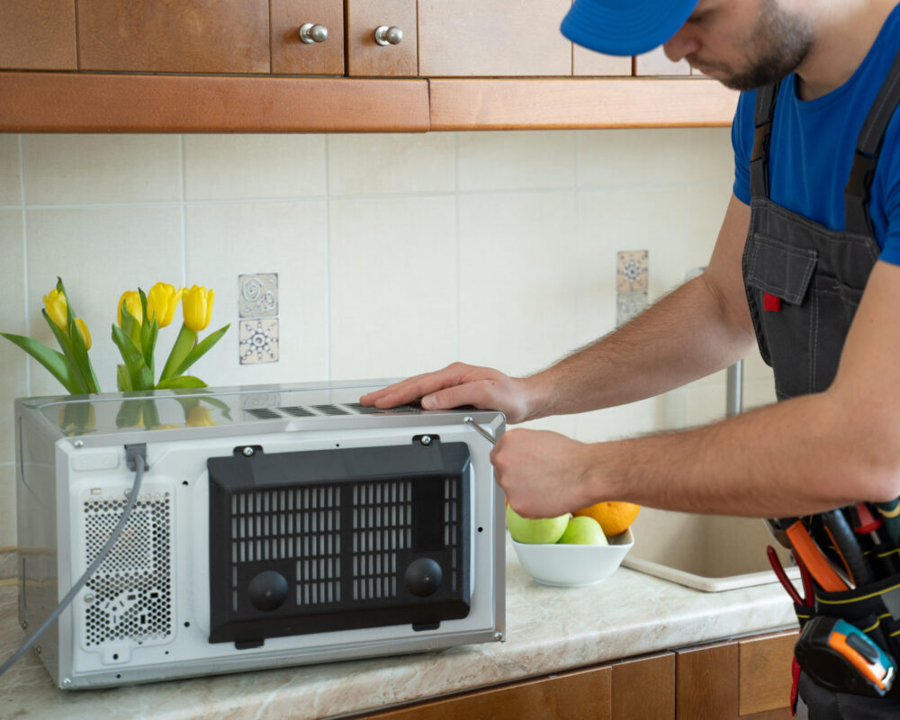 Young repairman fixing and repairing microwave oven by screwdriver in kitchen.